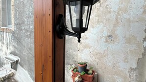 A wooden door with a black lantern hanging on the wall, a window, and a small shelf with potted plants. - Vacation house with Terrace in the historic center of Bernalda, 10 minutes from the sea. (Bernalda)