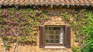 A stone building with a window and shutters, surrounded by greenery and flowering plants. - Elite Collection Molara Infinity Pool & View (Porto San Paolo)