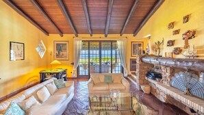 A spacious living room with a wooden ceiling, a sofa set, a glass coffee table, and a stone fireplace. - Elite Collection Molara Infinity Pool & View (Porto San Paolo)