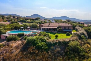 Una villa con piscina, rodeada de exuberante vegetación y montañas al fondo.