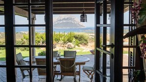 An open patio with a table and chairs, a hanging light fixture, and a view of a mountainous landscape. - Elite Collection Molara Infinity Pool & View (Porto San Paolo)