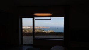 Een kamer met een groot raam met uitzicht op zee en verre gebouwen.
