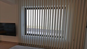 Een kamer met een bed, een aan de muur bevestigde televisie en een raam met verticale jaloezieën.