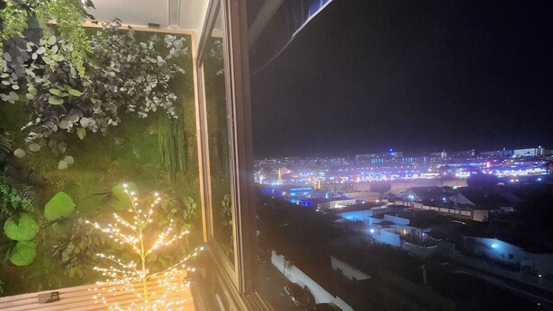 A balcony with a view of a cityscape at night, featuring illuminated buildings and a green wall with plants. - Luxury Apartment Very Close to the C.C. Yumbo with 2 King Size Beds 200x200cm (Maspalomas)