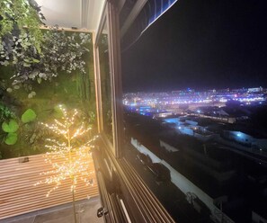 Uma varanda com vista para um horizonte urbano à noite, com edifícios iluminados e uma parede verde com plantas.