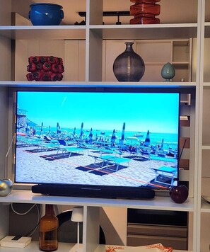 Un téléviseur diffusant une scène de plage, un pot bleu, un objet décoratif rouge et un vase, le tout placé sur des étagères.