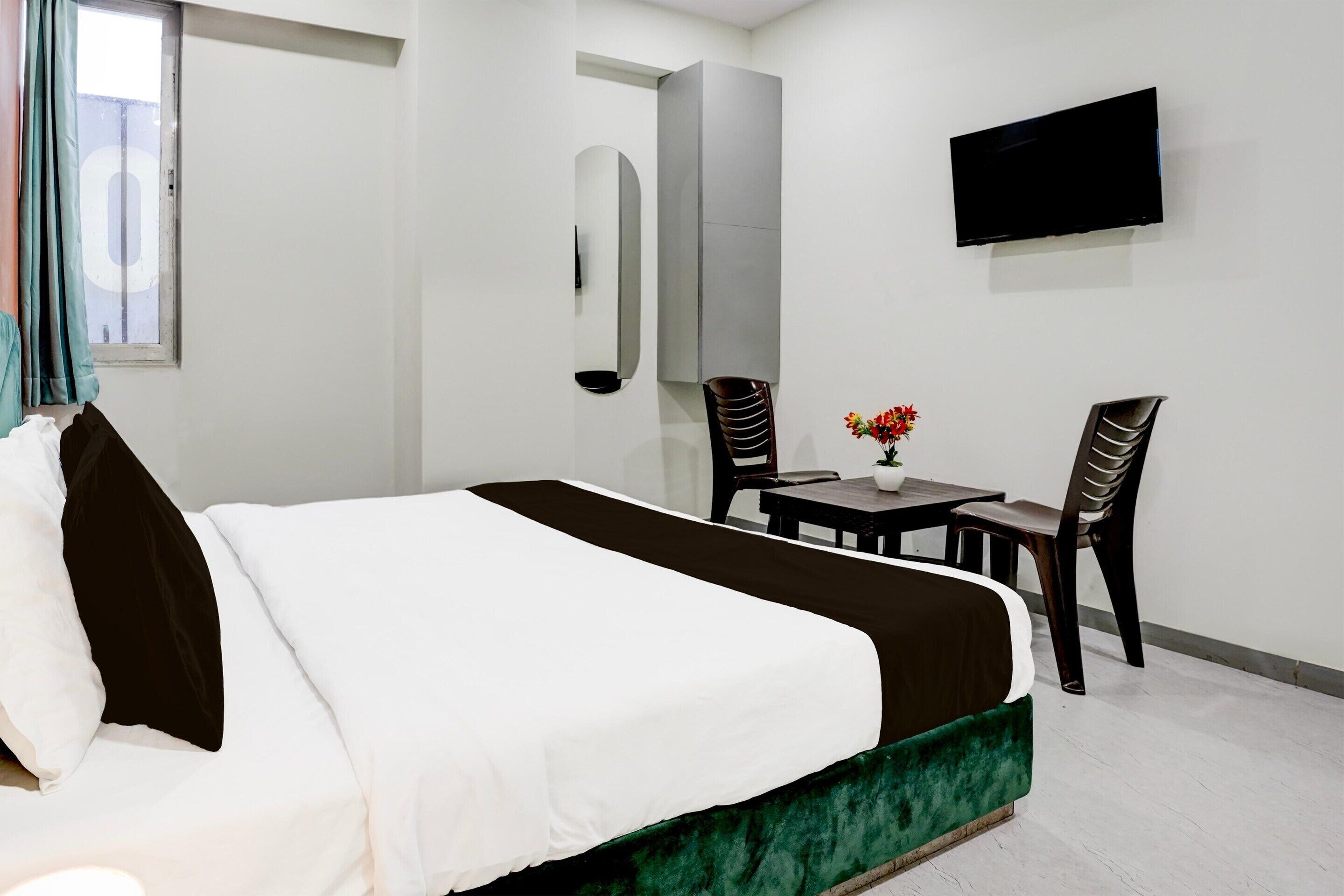 Une chambre d’hôtel comprenant un lit, une télévision, un bureau avec des chaises et une fenêtre avec des rideaux.