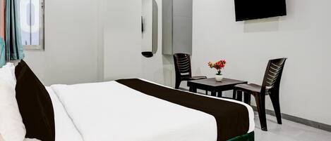 A hotel room with a bed, a TV, a desk with chairs, and a window with curtains.