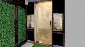 A modern entrance with a glass door, a green wall, and a small artificial grass area. - Deluxe Room Adajan Sky Palace (Surat)