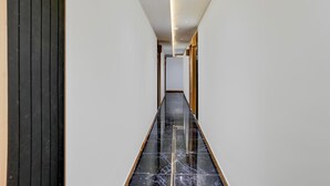 A hallway with a black marble floor, white walls, and a door marked '411'. - Deluxe Room Adajan Sky Palace (Surat)