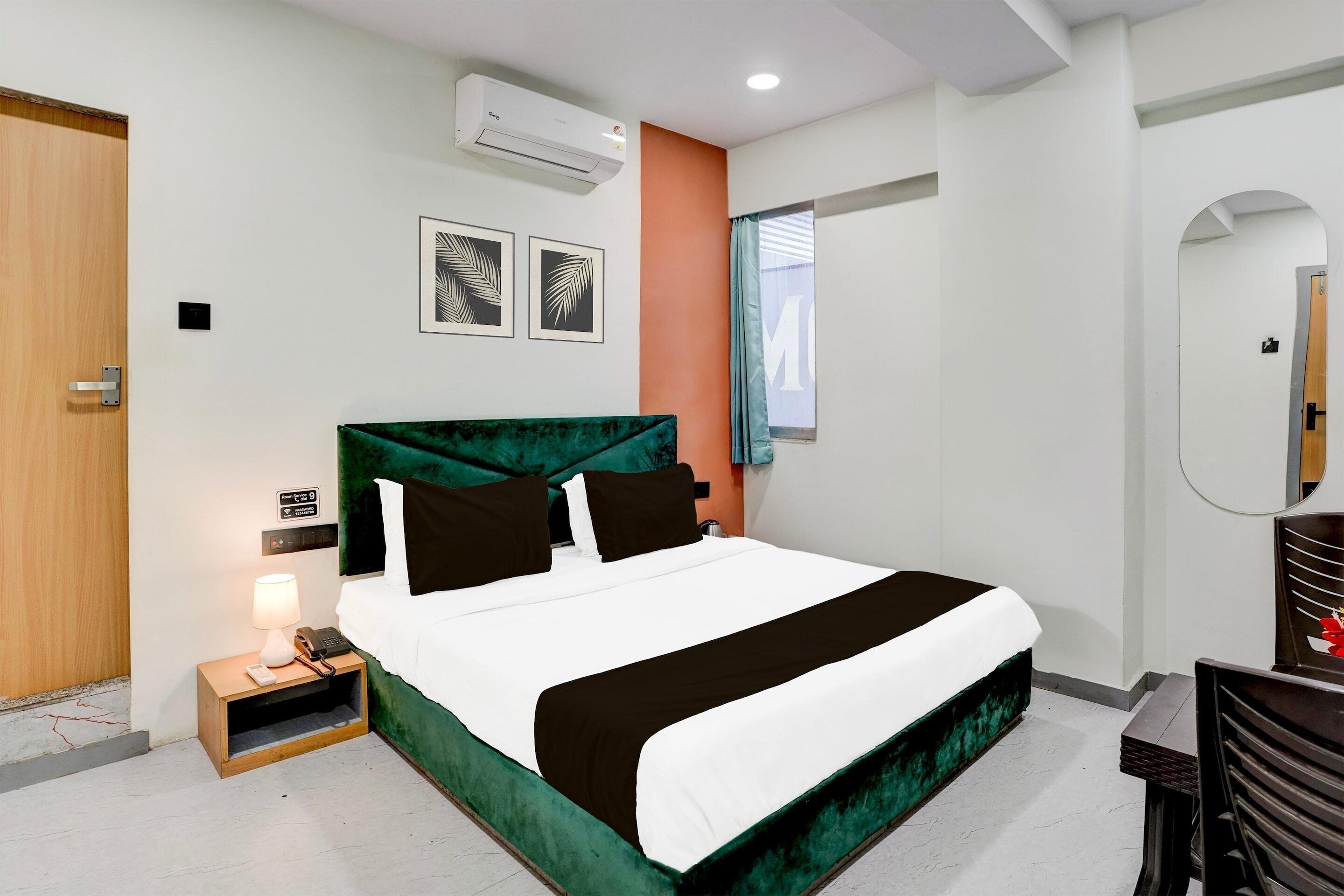 A hotel room with a bed, bedside table, lamp, and air conditioning unit.