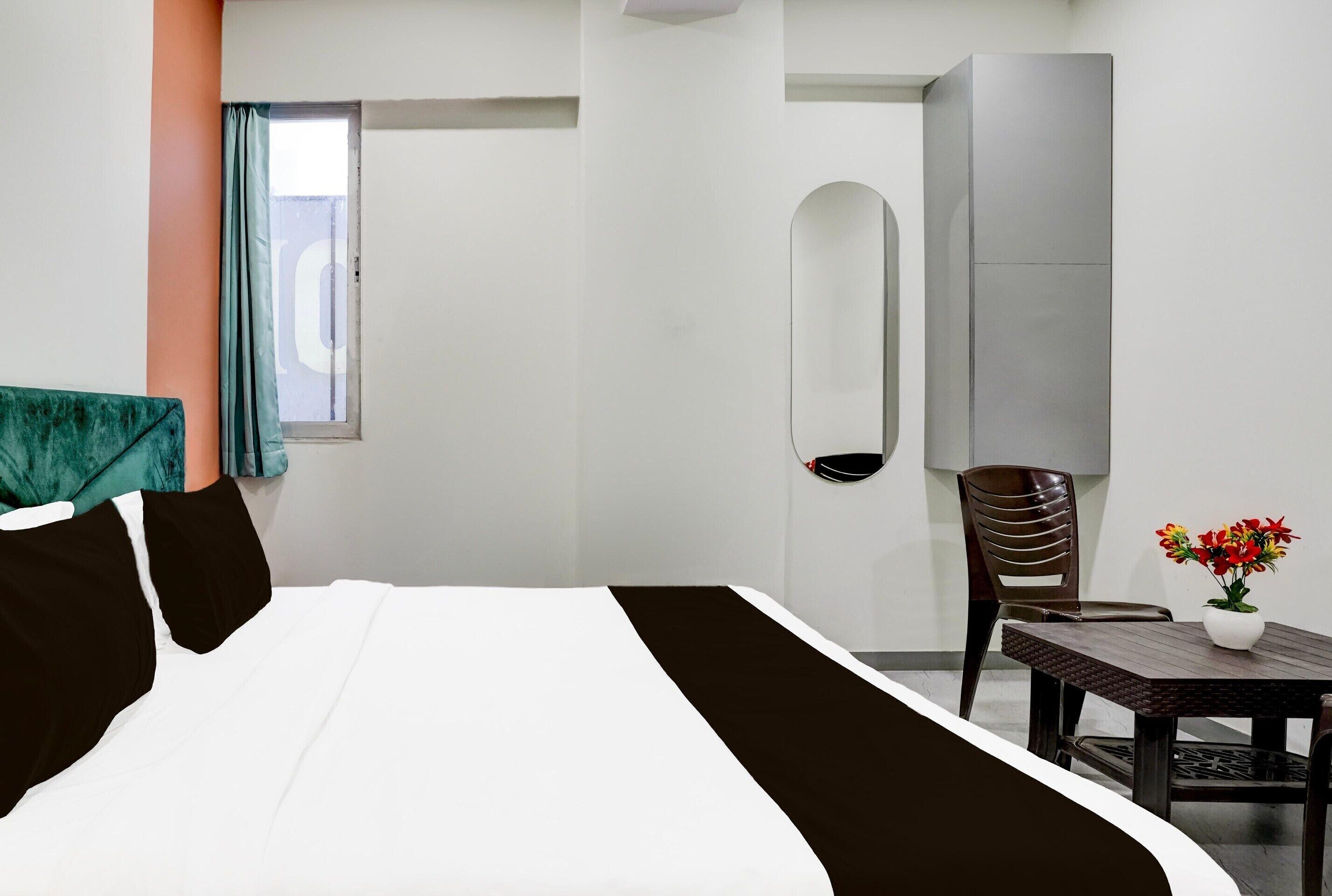 Ein Hotelzimmer mit Bett, einem Tisch mit Blumen, einem Sessel, einem Kleiderschrank und einem Fenster mit Vorhängen.