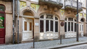 Un bâtiment historique doté de portes et de fenêtres blanches richement décorées, d’un pavé et d’une porte rouge sur le côté gauche.
