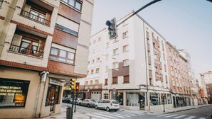 A street view with a multi-story building, a crosswalk, and parked cars. - Apartment with parking included (Gijon)