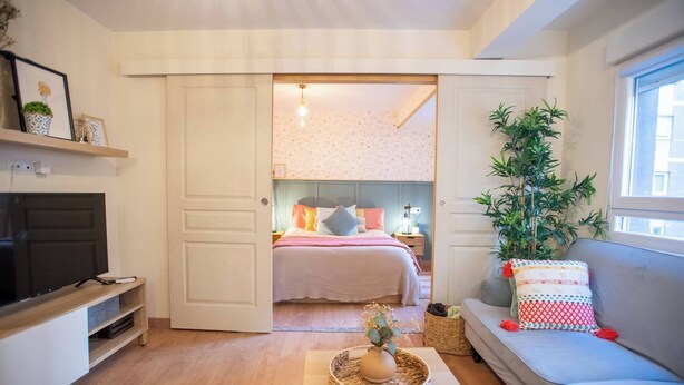 A modern apartment with a living room, a bedroom, a sofa, a TV, and a large window. - Apartment with parking included (Gijon)