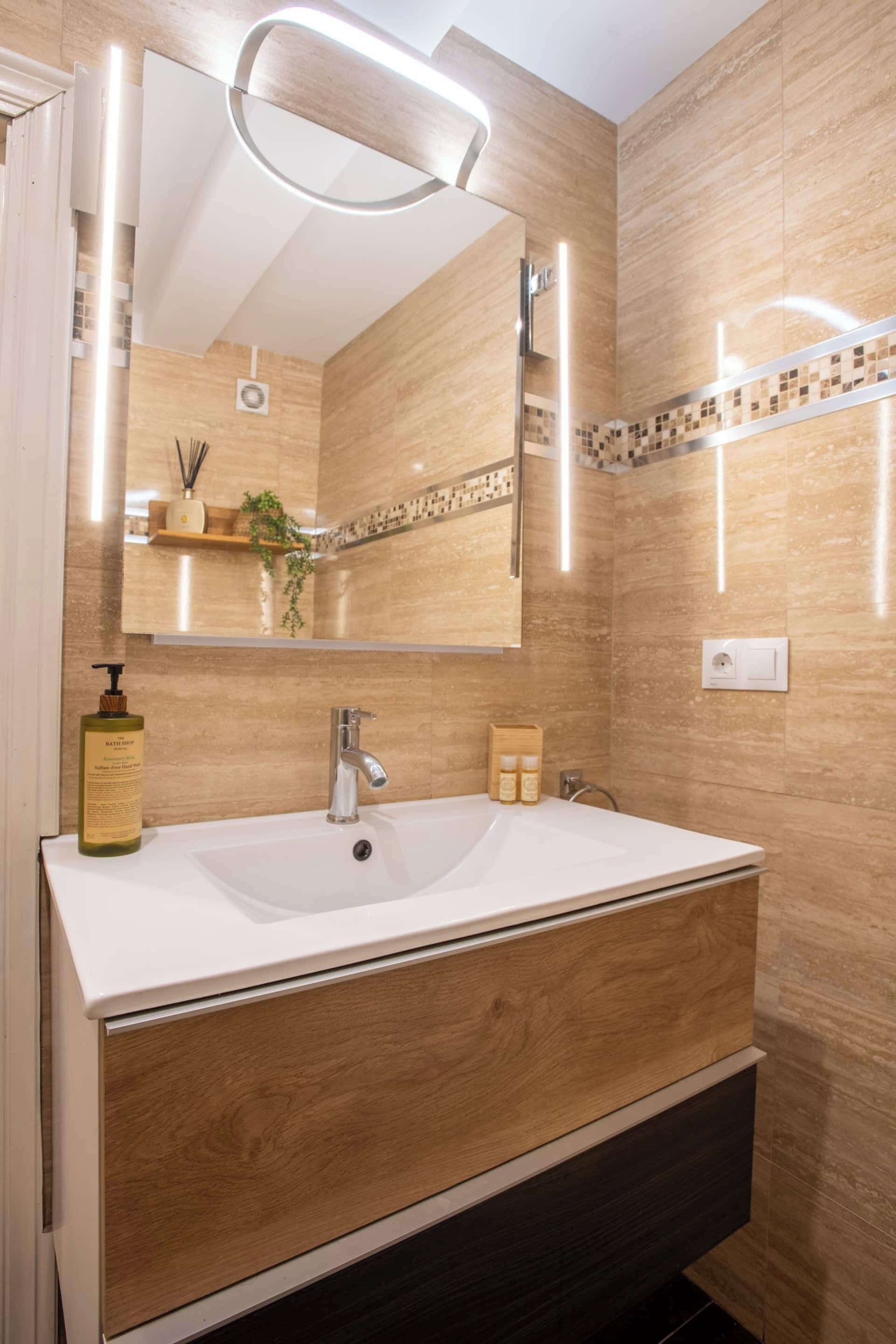 Une salle de bain moderne avec un grand miroir, un lavabo blanc, un meuble-lavabo en bois et une petite étagère contenant des articles de toilette.