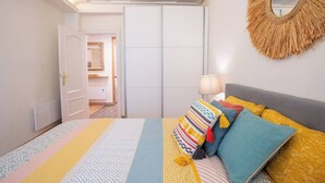 A bedroom with a bed, a bedside lamp, a mirror, and a door leading to another room. - Apartment with parking included (Gijon)
