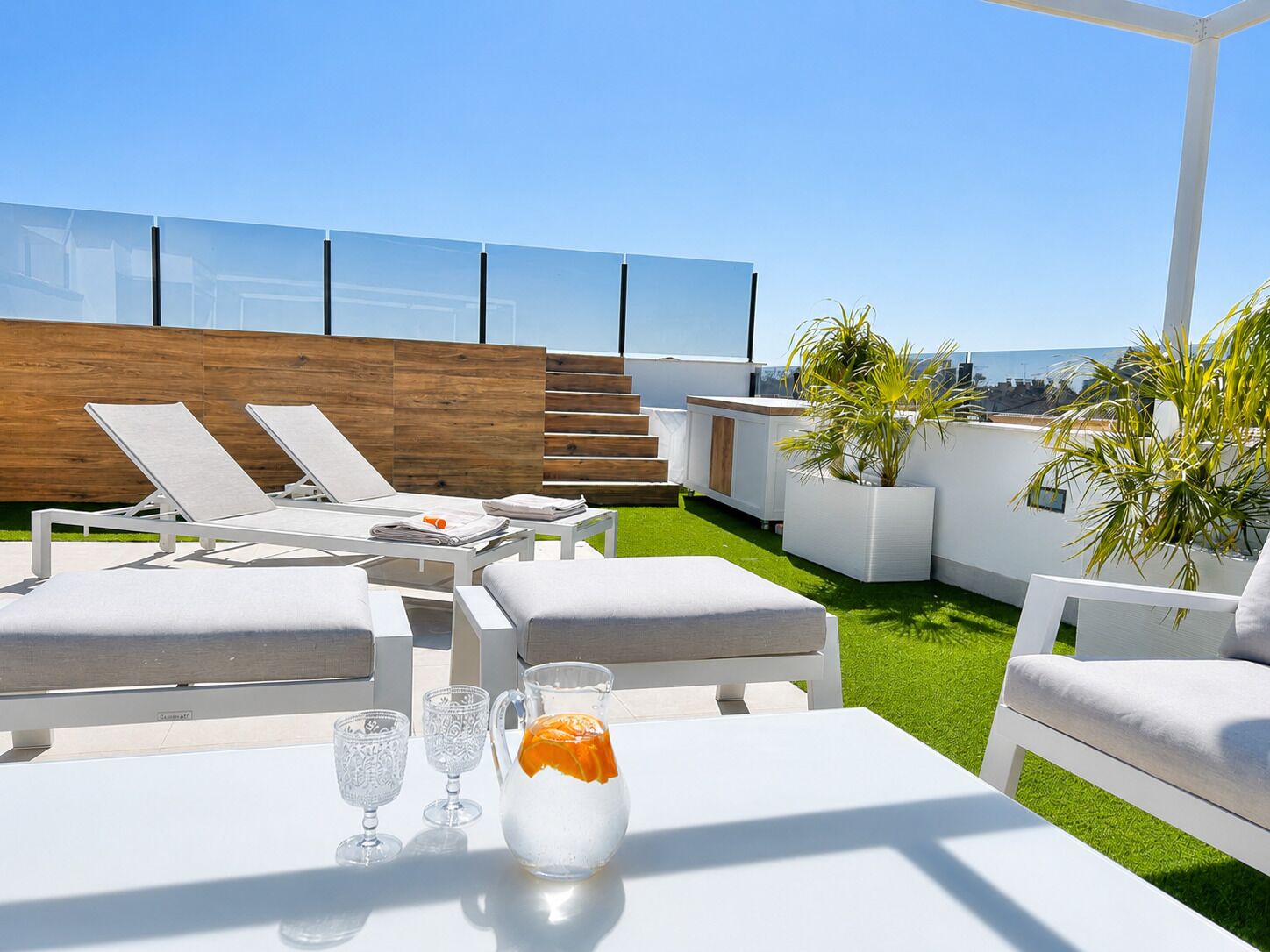 A rooftop terrace with lounge chairs, a table with glasses and a pitcher, and a view of the city.