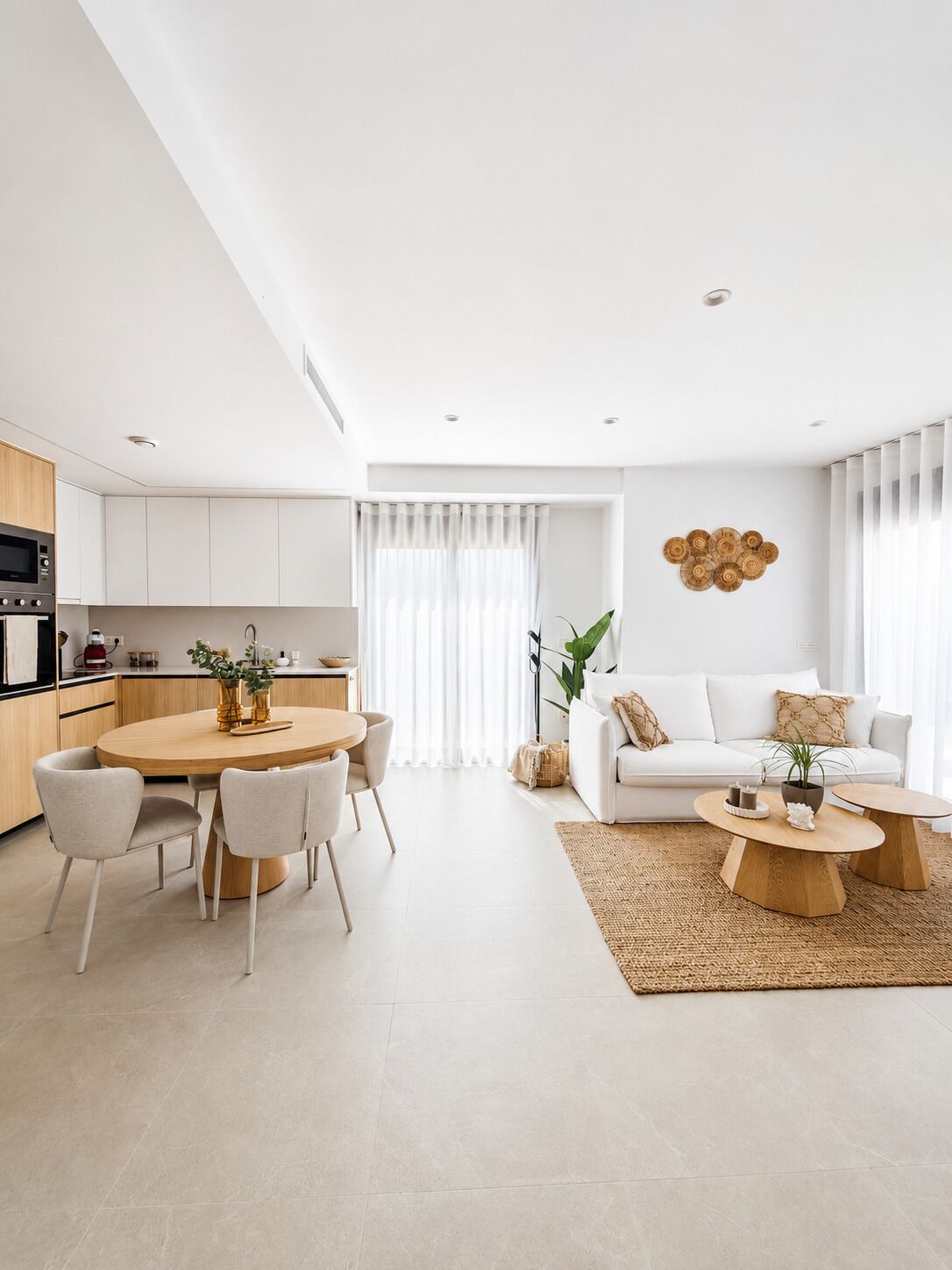 A modern kitchen with white cabinetry, a dining area with a round table and chairs, and a living room with a white sofa and a coffee table.