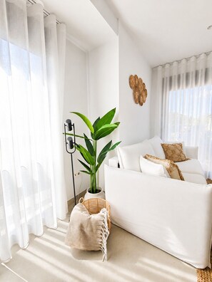 A modern living room with a white sofa, a potted plant, and a wall-mounted light fixture. - Casa Aruna | Private Pool & Rooftop Terracel (San Pedro del Pinatar)