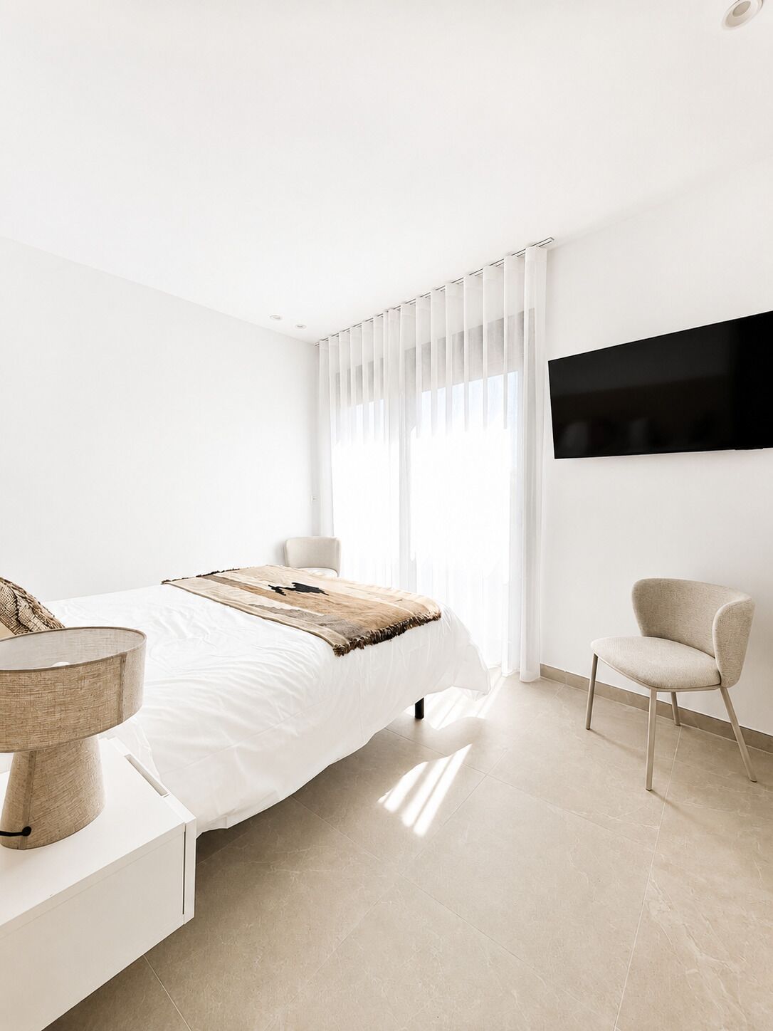 Um quarto moderno com cama, mesa de cabeceira, cadeira e televisão na parede.