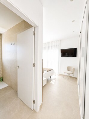 Een moderne slaapkamer met een bed, een stoel en een aan de muur bevestigde televisie.