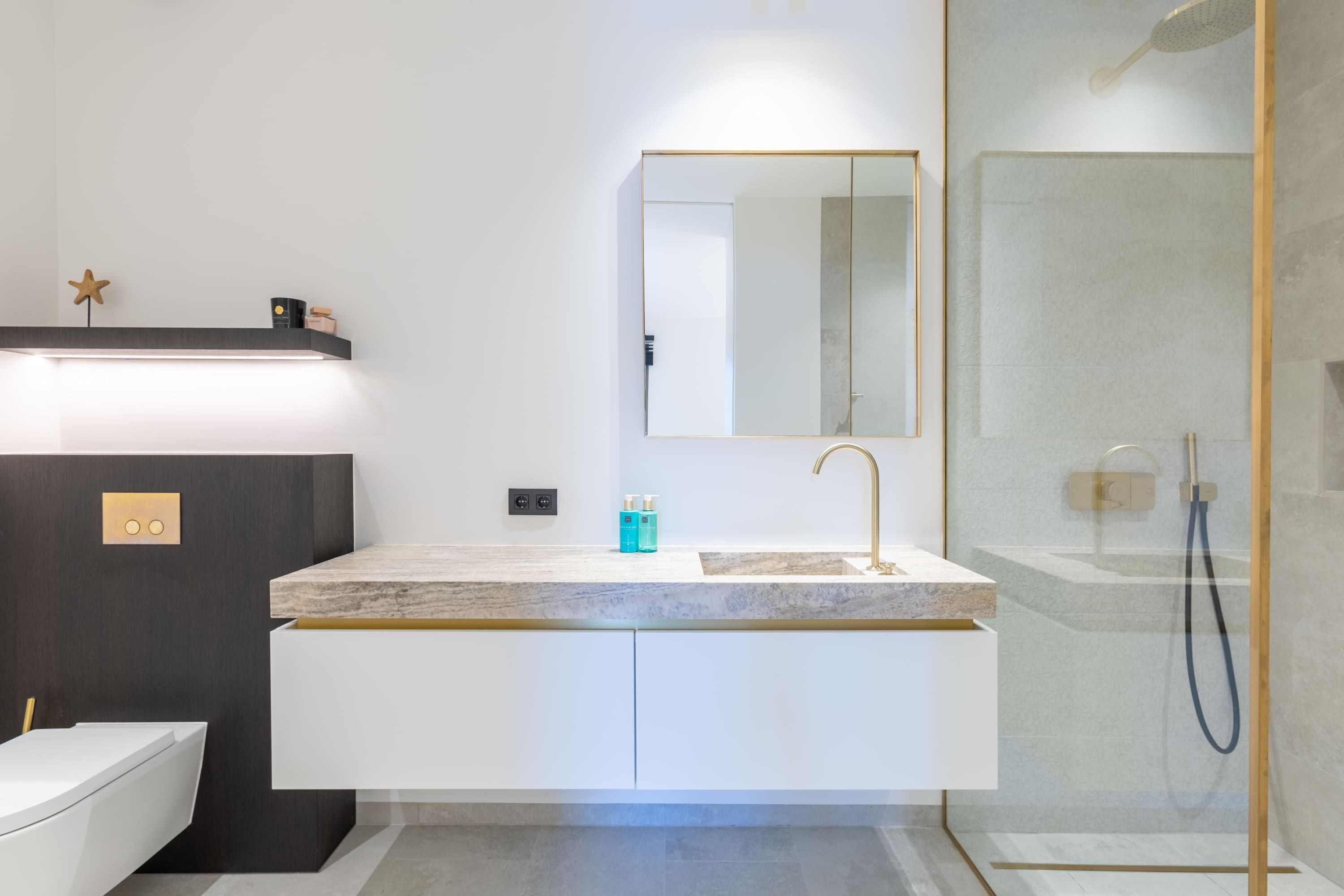 Un baño moderno con tocador blanco, grifo dorado y cabina de ducha de vidrio.