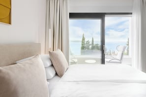 Een hotelkamer met een bed, uitzicht op zee en een balkon met stoelen.