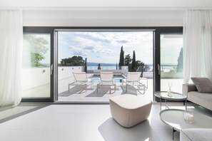 Een moderne woonkamer met een grote schuifpui naar een balkon met een zwembad en buitenmeubilair.