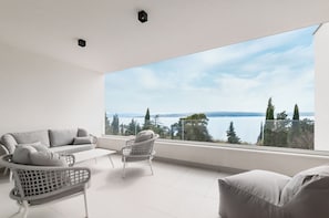 Een moderne kamer met een groot raam, een bank, twee rieten stoelen en uitzicht op een meer en bomen.