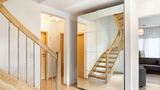 Un interior moderno con una escalera de madera, un muro espejado y una sala de estar con sofá.