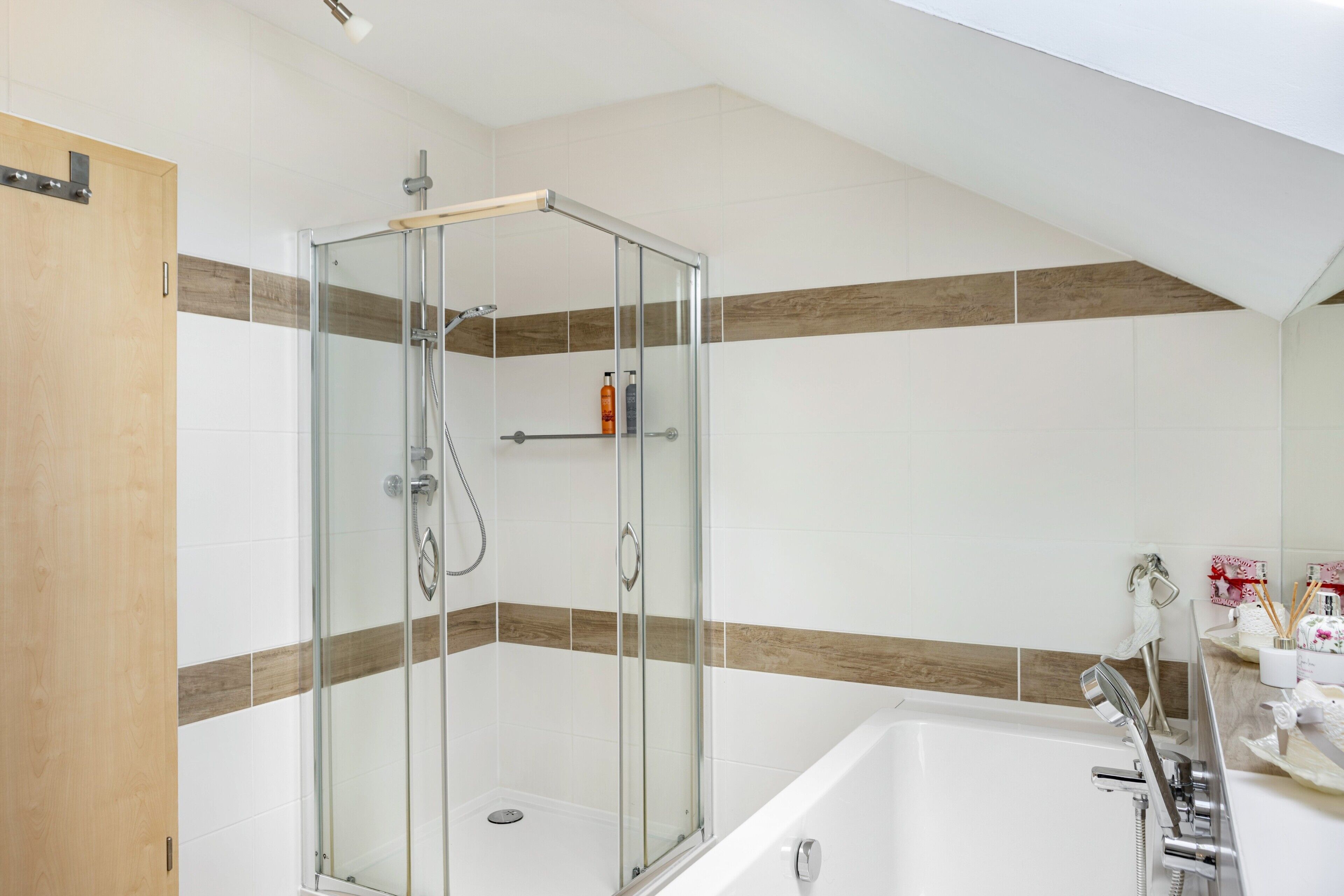 A modern bathroom with a glass-enclosed shower, a bathtub, and a wooden door.