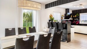 Un comedor moderno con mesa y sillas, una cocina con televisor de pantalla plana y vistas a zonas verdes exteriores.