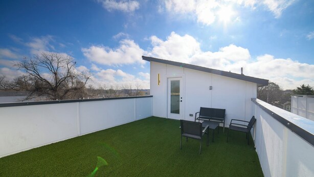 A rooftop terrace with artificial grass, a small white building, and two chairs. - House of Tranquility (Dallas)
