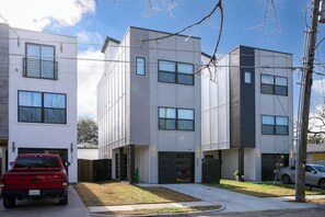 Um edifício residencial moderno de vários andares, com garagem, entrada para carros e um pequeno jardim frontal.