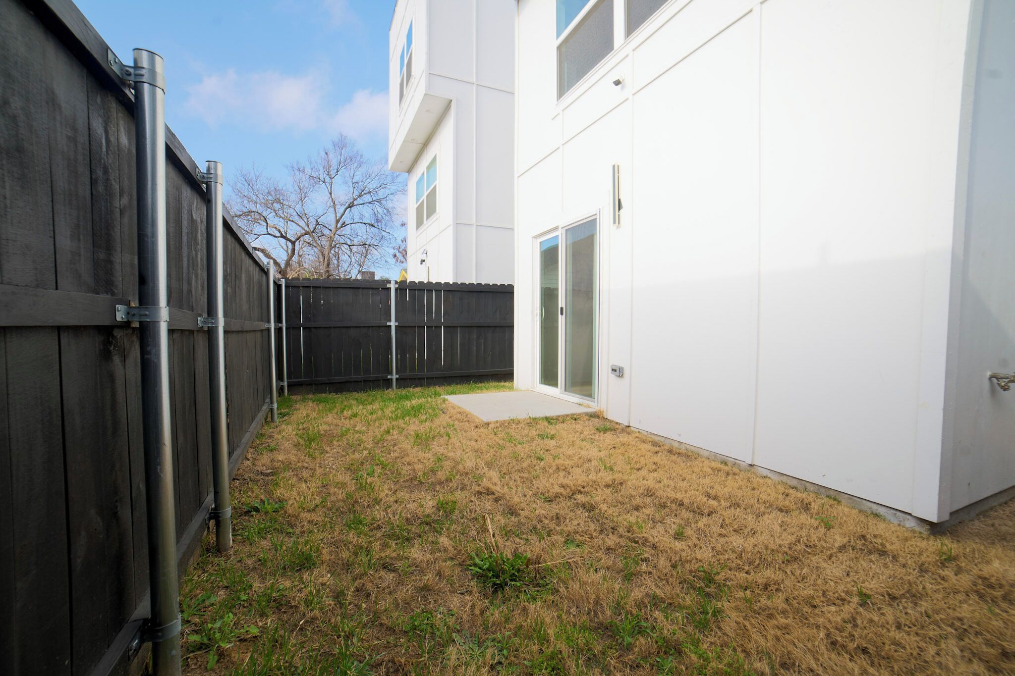 A backyard with a wooden fence, a white building with a glass door, and a clear sky.