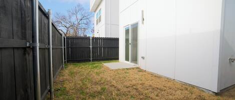 A backyard with a wooden fence, a white building with a glass door, and a clear sky.