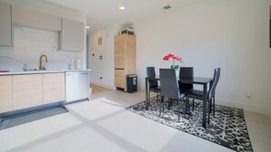 A modern kitchen with a dishwasher, a wooden cabinet, and a dining area with a table and chairs. - House of Tranquility (Dallas)
