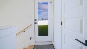 A white door with a view of a grassy field and a clear sky. - House of Tranquility (Dallas)