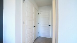 A hallway with white doors and a carpeted floor. - House of Tranquility (Dallas)