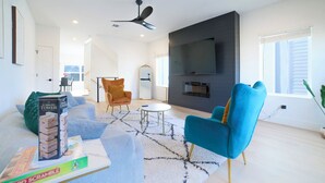 A modern living room with a flat-screen TV, a ceiling fan, and a fireplace. - House of Tranquility (Dallas)