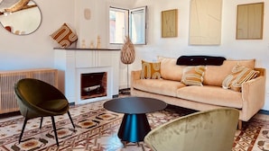 Uma sala de estar com sofá, cadeiras, mesa de centro redonda, lareira e obras de arte nas paredes.