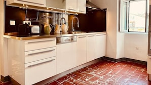Uma cozinha moderna com armários brancos, eletrodomésticos de aço inoxidável e chão com ladrilhos vermelhos.