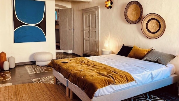 Quarto com cama, almofadas, luminária na parede e porta.