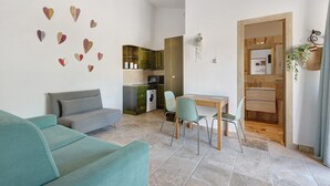 A living room with a sofa, a dining table with chairs, a kitchen area, and a bathroom visible through an open door. - Holiday Home 'Kim' with Private Garden, Wi-Fi and Air Conditioning (Capoliveri)