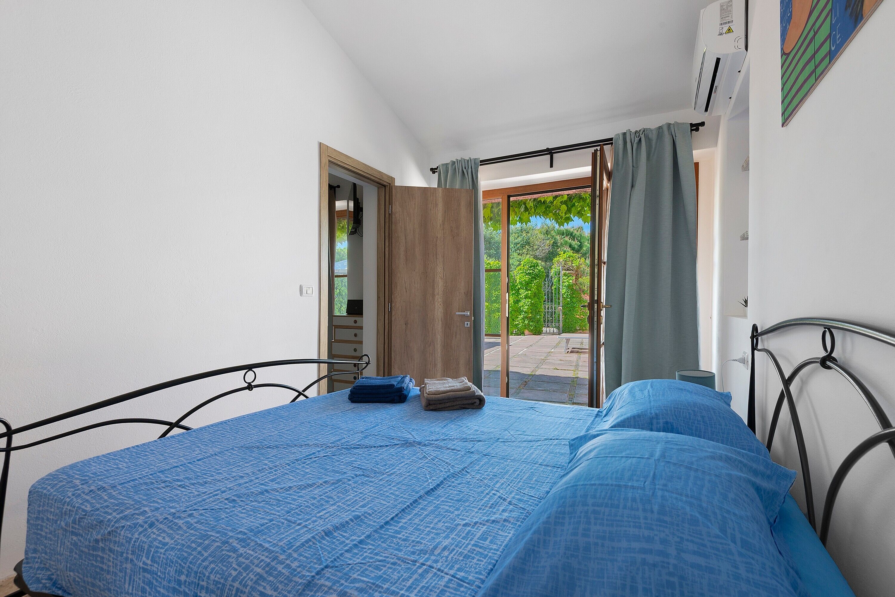 Ein Schlafzimmer mit Bett, einem Fenster mit Vorhängen, einer Tür und einer Klimaanlage.