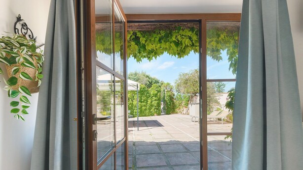 A sliding glass door leading to an outdoor patio area with a stone floor, a metal grate, and a hanging plant. - Holiday Home 'Kim' with Private Garden, Wi-Fi and Air Conditioning (Capoliveri)
