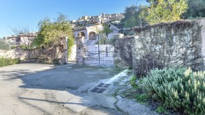 A paved area with a gated entrance, a stone wall, and a hillside with buildings. - Holiday Home 'Kim' with Private Garden, Wi-Fi and Air Conditioning (Capoliveri)