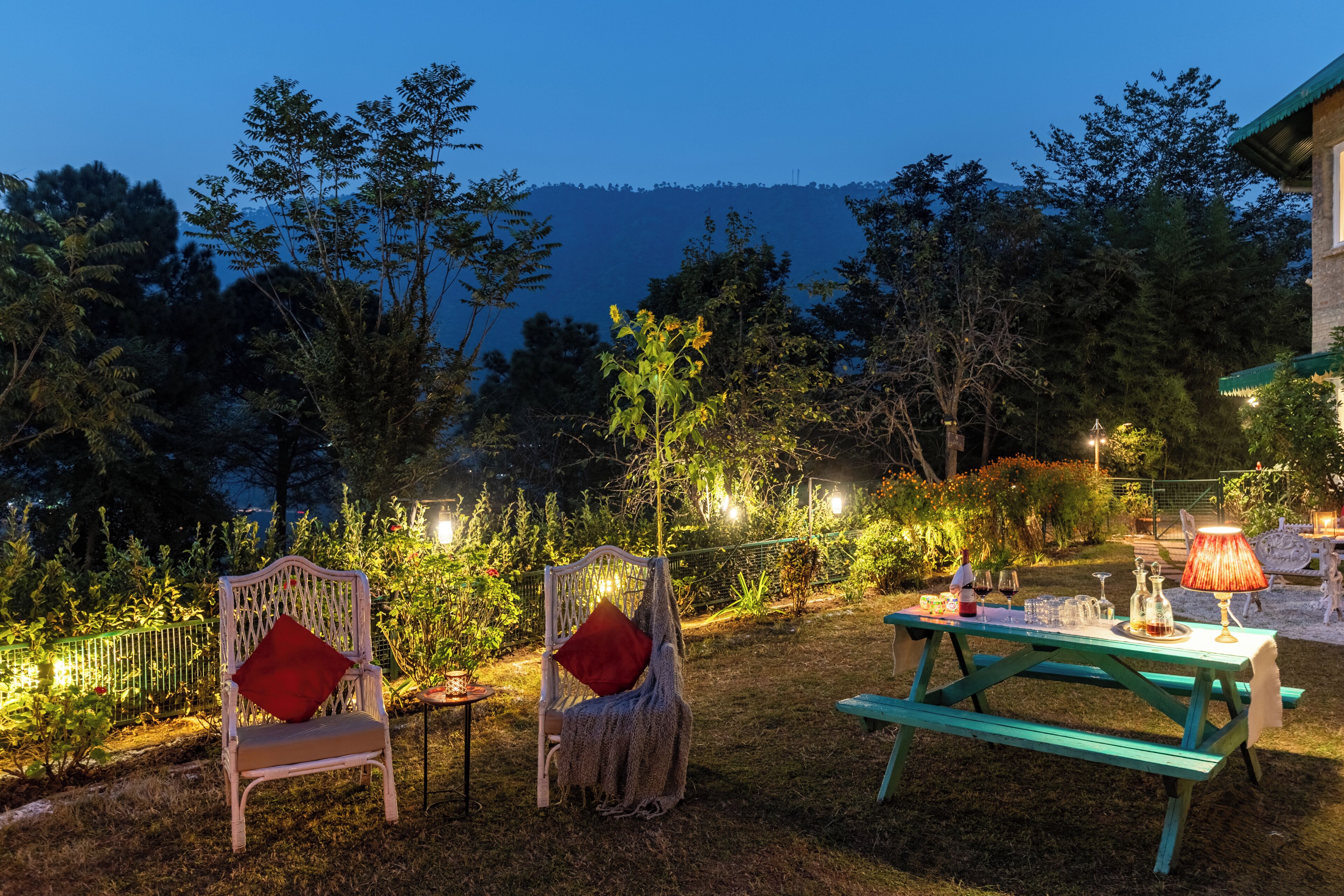 A patio with two chairs, a table with a lamp, and a view of a forested hill.