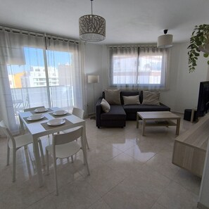 A modern living room with a dining area, a sofa, a coffee table, and a TV. - Apartamento Ponent Inmomart (Peñiscola)